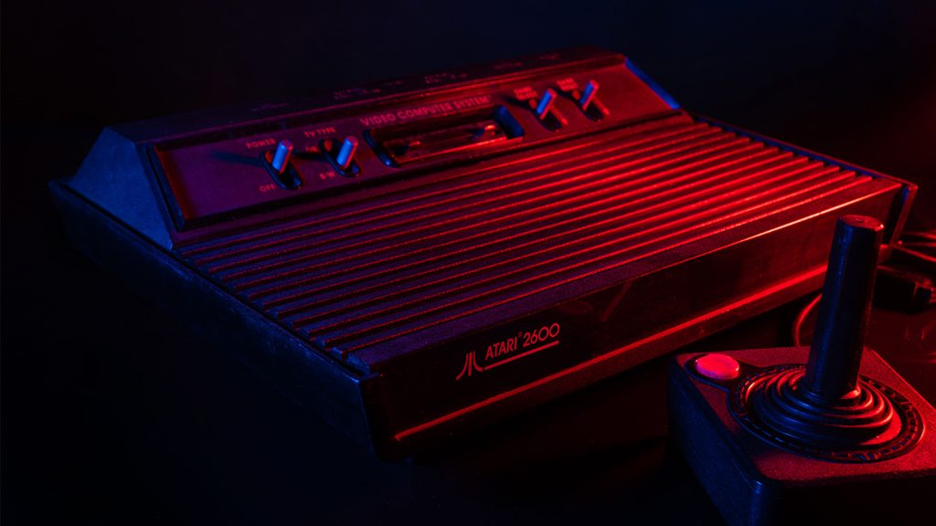 Atari 2600 "VCS" game system from 1977, displayed in low red light with a joystick controller.