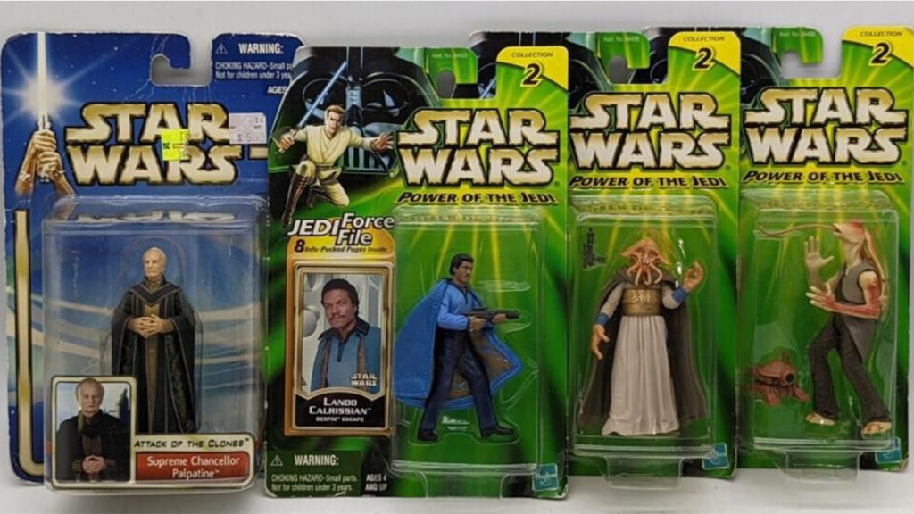 One action figure in blue packaging and three figures in green packaging propped on a white surface.